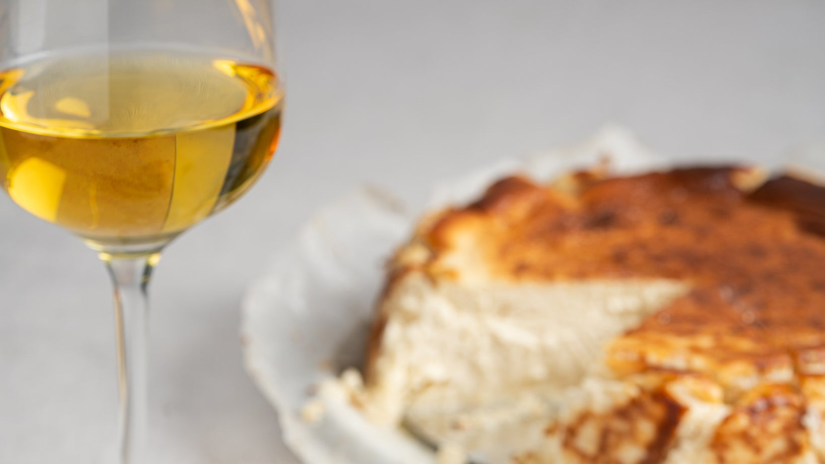Slice of Basque burnt cheesecake with a glass of Basque sweet wine on a light gray surface